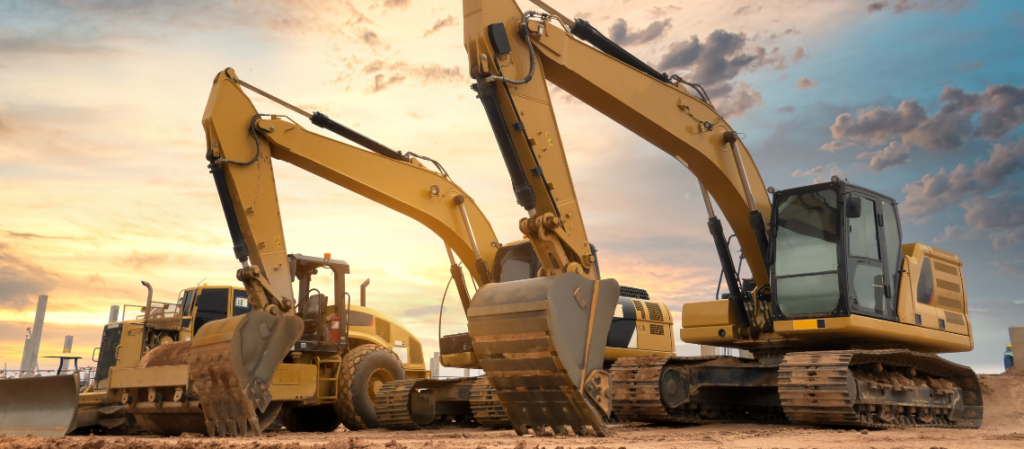 Two large excavators and a bulldozer at a construction site during sunset.