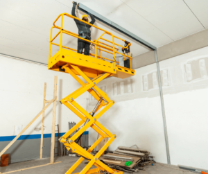 Yellow scissor lift in use inside of a construction site.