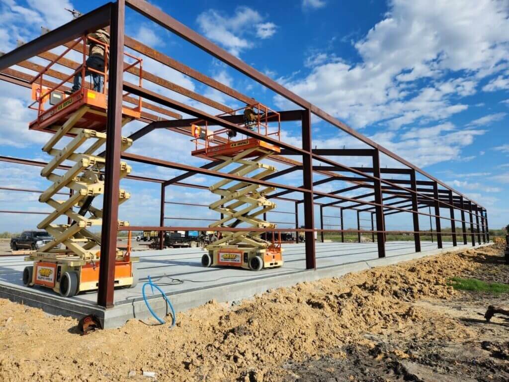 Pair of orange and yellow scissor lifts in use on a construction site of a building.